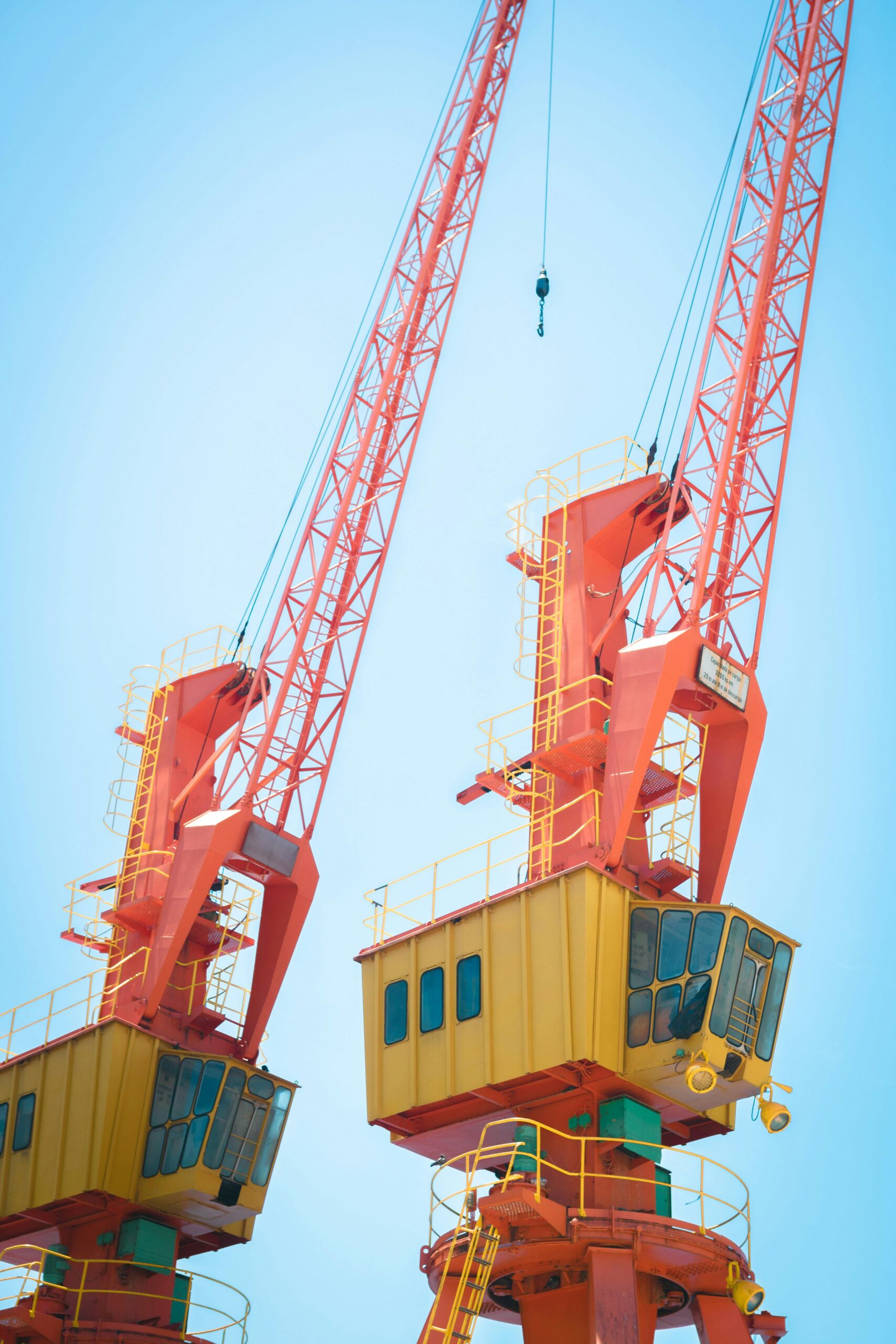 Two vibrant orange cranes under a clear blue sky, symbolizing modern industry and construction.